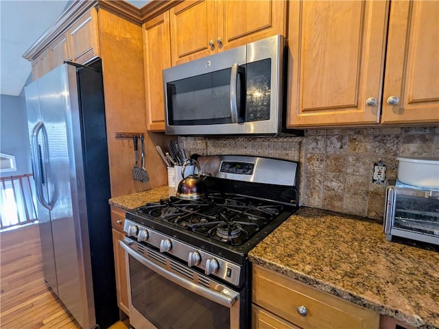 kitchen featuring stainless steel appliances, decorative backsplash, and dark stone countertops