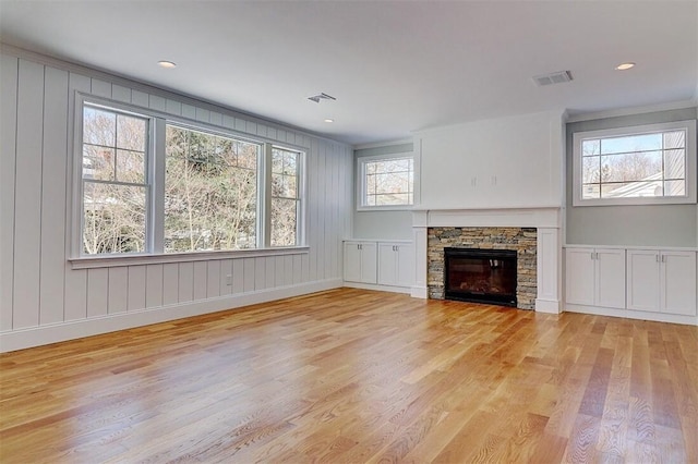 unfurnished living room featuring crown molding, a stone fireplace, and light wood-type flooring