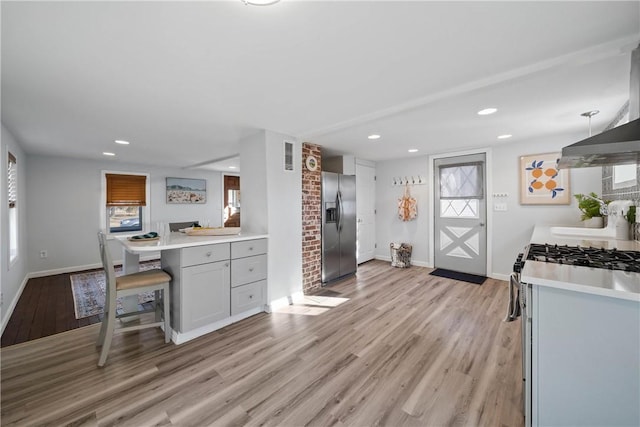 kitchen featuring light hardwood / wood-style flooring, a breakfast bar area, gray cabinets, appliances with stainless steel finishes, and decorative light fixtures