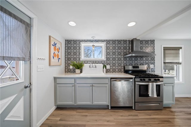 kitchen featuring plenty of natural light, appliances with stainless steel finishes, sink, and wall chimney range hood