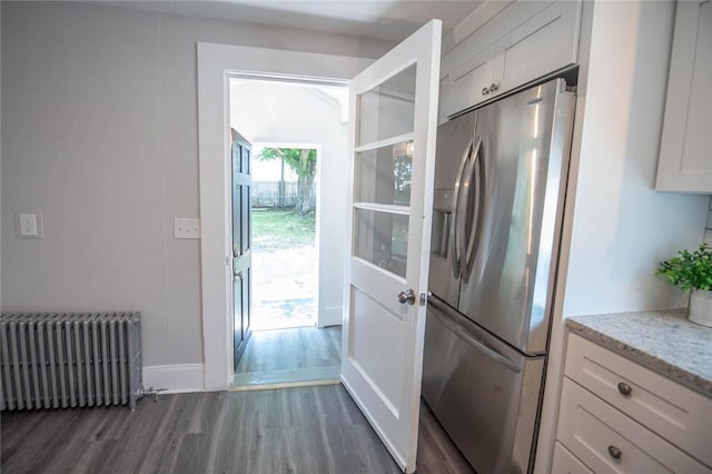 kitchen featuring radiator heating unit, dark hardwood / wood-style floors, stainless steel fridge, light stone countertops, and white cabinets