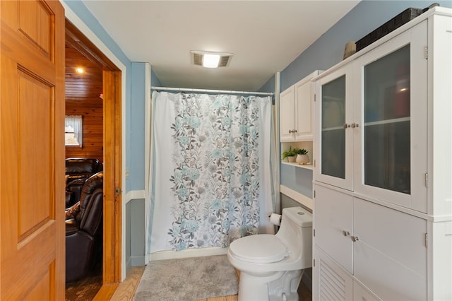 bathroom with wooden walls, toilet, and a shower with shower curtain