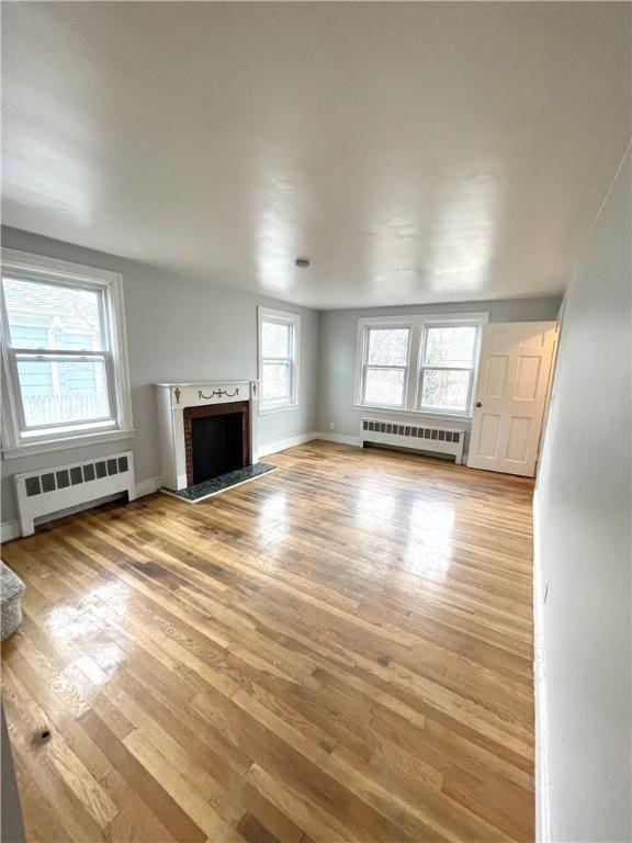 unfurnished living room with radiator heating unit, a fireplace, and light hardwood / wood-style floors