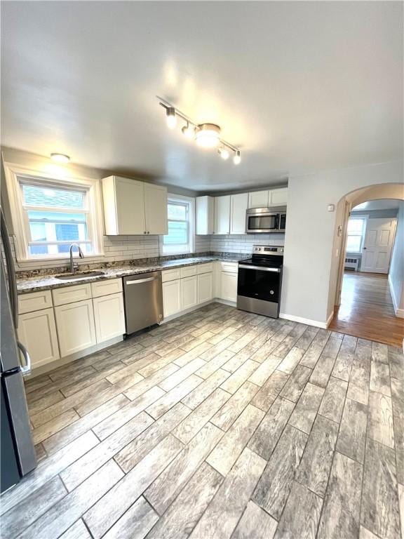 kitchen featuring sink, backsplash, appliances with stainless steel finishes, light hardwood / wood-style floors, and white cabinets