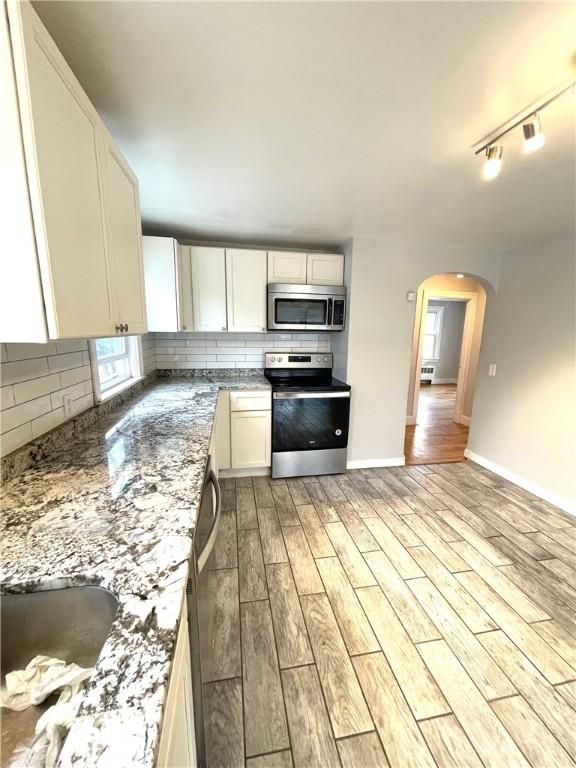 kitchen featuring appliances with stainless steel finishes, white cabinetry, backsplash, stone countertops, and light wood-type flooring