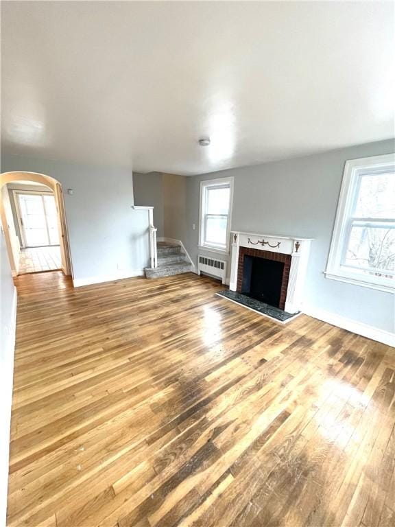 unfurnished living room featuring a brick fireplace, radiator heating unit, and light hardwood / wood-style floors