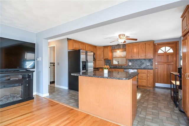 kitchen with sink, stainless steel fridge, a kitchen island, decorative backsplash, and dark stone counters