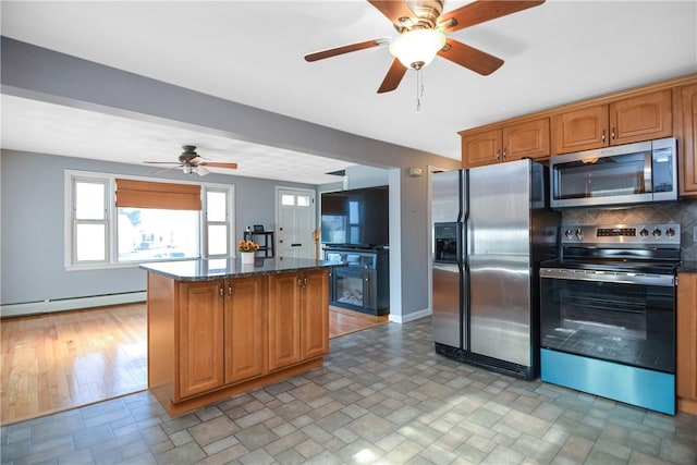 kitchen featuring baseboard heating, dark stone countertops, backsplash, appliances with stainless steel finishes, and a kitchen island