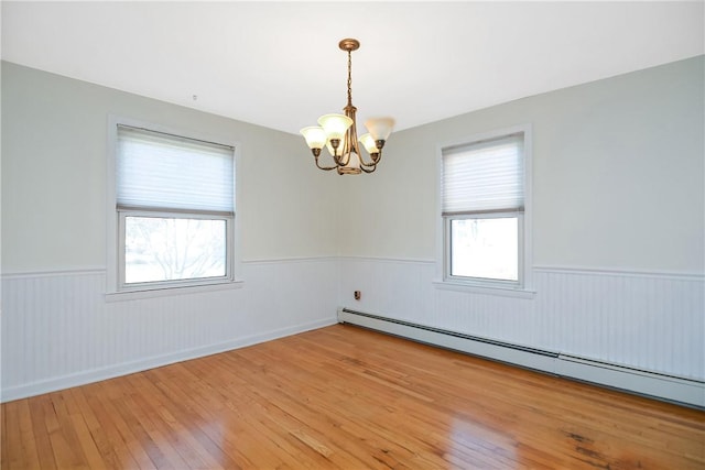 empty room with an inviting chandelier, a baseboard heating unit, and hardwood / wood-style floors