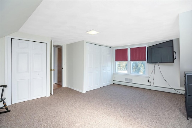 unfurnished bedroom featuring a baseboard heating unit, multiple closets, and carpet flooring