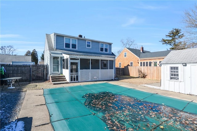 back of house with a sunroom, a covered pool, and a storage unit