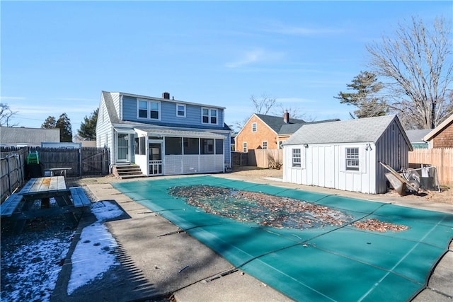 rear view of house featuring an outbuilding, a sunroom, a covered pool, and a patio area