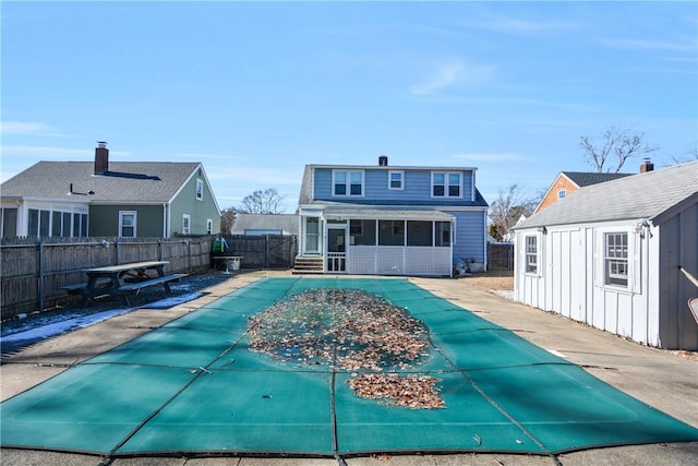 back of property featuring an outdoor structure, a sunroom, a patio, and a covered pool