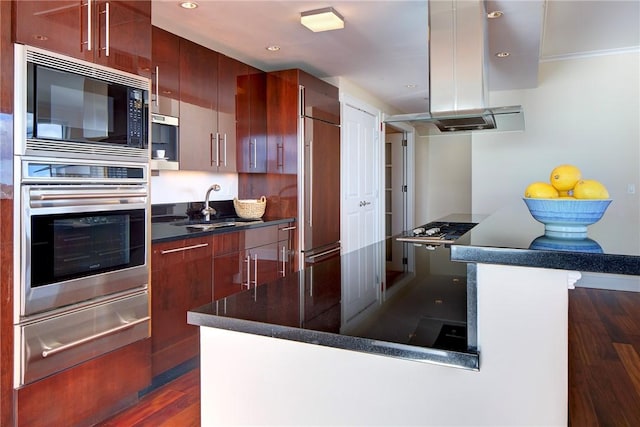 kitchen featuring island exhaust hood, sink, built in appliances, and dark hardwood / wood-style floors