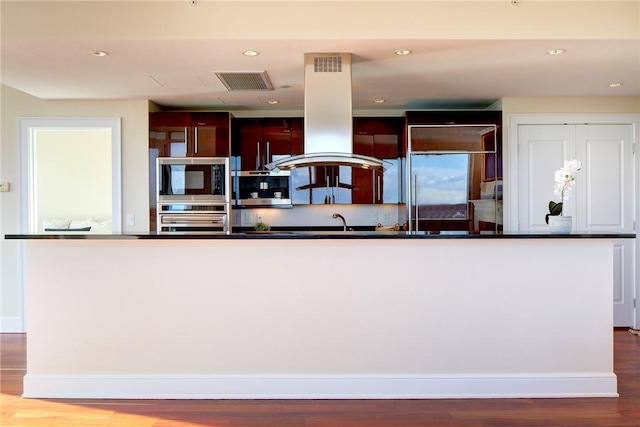 kitchen with island exhaust hood, a kitchen island, wood-type flooring, and built in appliances