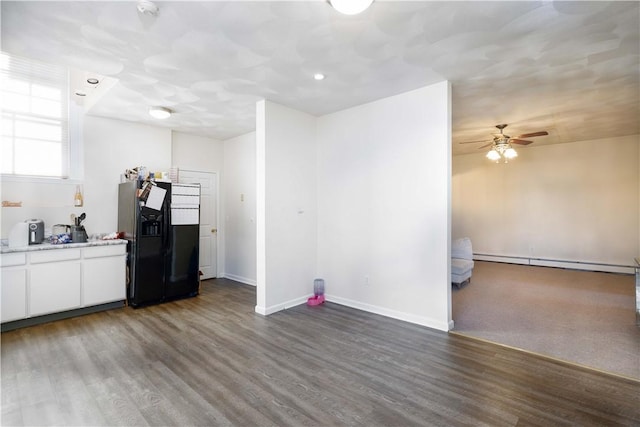 kitchen featuring white cabinetry, dark hardwood / wood-style flooring, a baseboard heating unit, ceiling fan, and black fridge