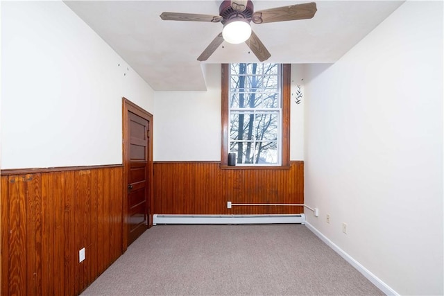 unfurnished room with a baseboard radiator, light carpet, ceiling fan, and wooden walls