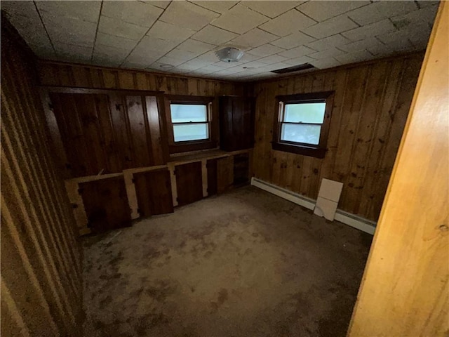 basement featuring wooden walls, a baseboard radiator, and carpet flooring