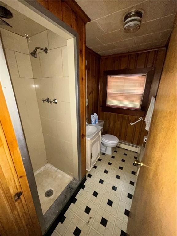 bathroom with baseboard heating, tiled shower, wooden walls, and toilet