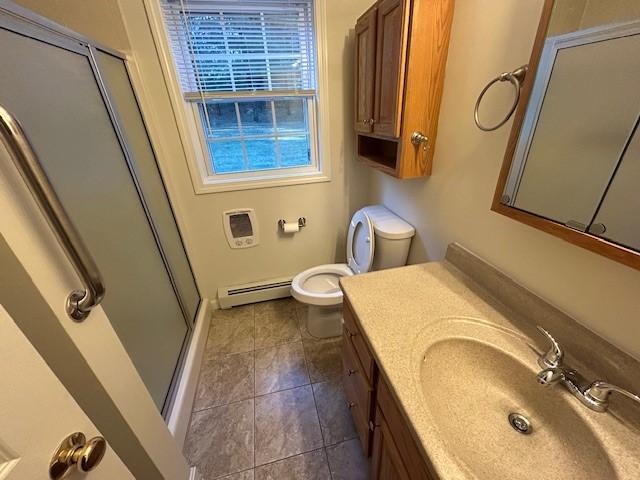 bathroom featuring vanity, baseboard heating, toilet, a shower with door, and tile patterned floors