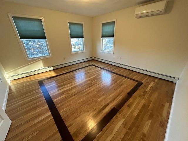 unfurnished room with a wall mounted air conditioner, a baseboard radiator, and hardwood / wood-style floors