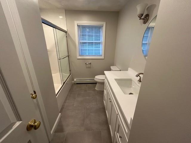 full bathroom with toilet, bath / shower combo with glass door, baseboard heating, vanity, and tile patterned flooring