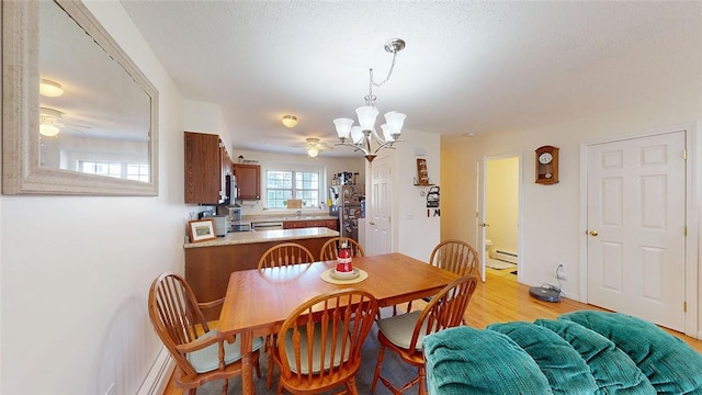 dining area featuring ceiling fan with notable chandelier, light wood-type flooring, a textured ceiling, and a baseboard heating unit