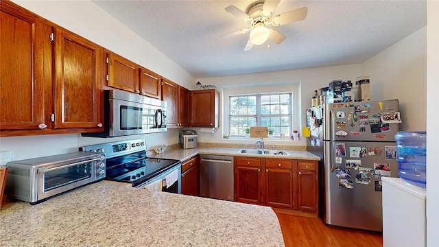 kitchen with sink, a textured ceiling, ceiling fan, stainless steel appliances, and light hardwood / wood-style floors