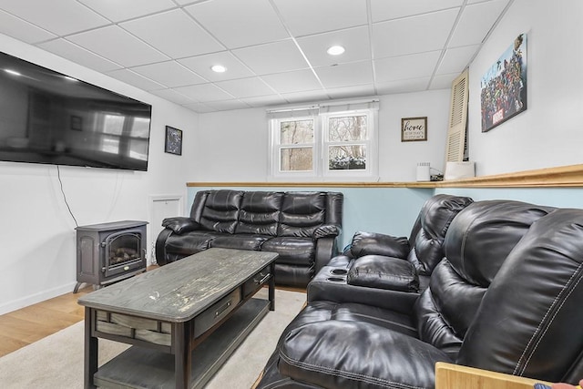 living room featuring a wood stove, a drop ceiling, and light hardwood / wood-style floors