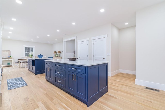 kitchen with blue cabinetry, a kitchen island, and light hardwood / wood-style flooring