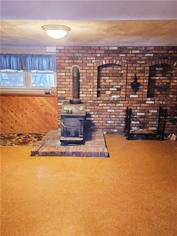 unfurnished living room with brick wall, a wood stove, wooden walls, and a textured ceiling