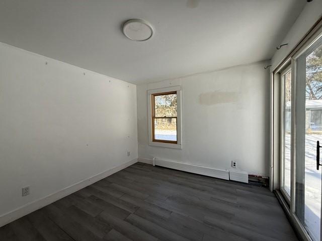 unfurnished room featuring dark hardwood / wood-style floors and a baseboard heating unit