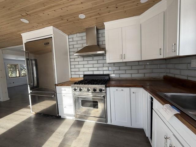 kitchen featuring white cabinetry, wall chimney range hood, wood counters, and high quality appliances