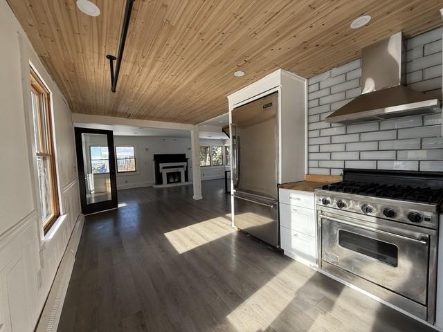 kitchen with high quality appliances, white cabinets, wood ceiling, dark wood-type flooring, and wall chimney exhaust hood