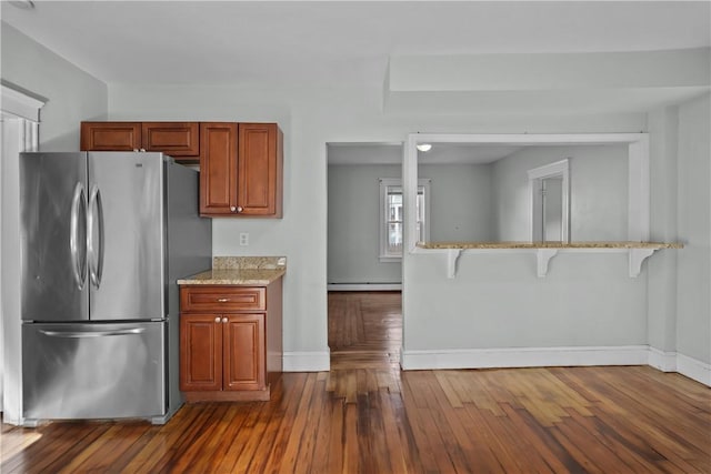 kitchen featuring dark wood-type flooring, a baseboard radiator, stainless steel refrigerator, and a kitchen bar