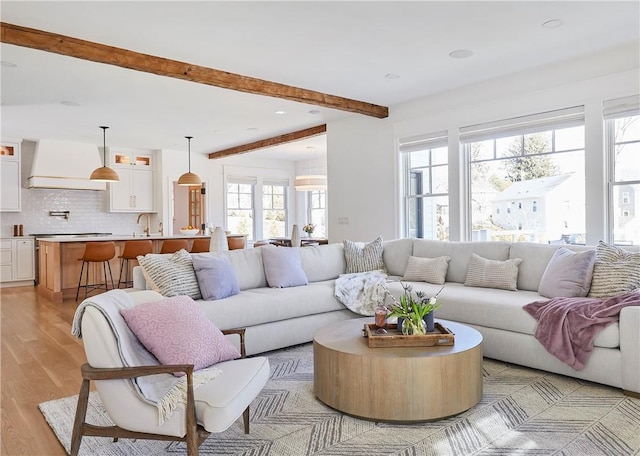 living room with sink, beam ceiling, and light wood-type flooring