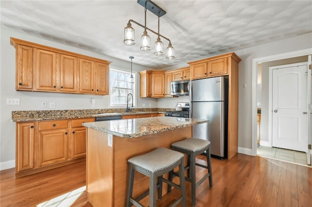 kitchen with stainless steel appliances, a center island, light stone countertops, decorative light fixtures, and light wood-type flooring