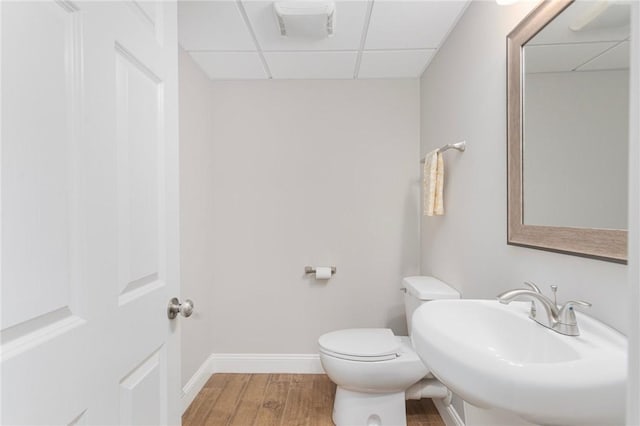 half bathroom featuring a drop ceiling, toilet, wood finished floors, a sink, and baseboards