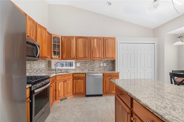 kitchen with lofted ceiling, light stone counters, a sink, appliances with stainless steel finishes, and glass insert cabinets