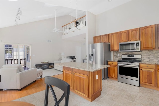 kitchen featuring light stone countertops, appliances with stainless steel finishes, open floor plan, and brown cabinetry