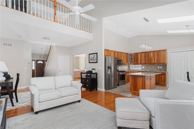 living area featuring ceiling fan, high vaulted ceiling, a skylight, visible vents, and light wood-type flooring