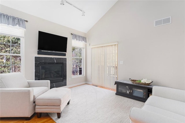 living room featuring high vaulted ceiling, a healthy amount of sunlight, visible vents, and a premium fireplace