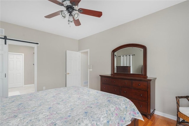 bedroom with ceiling fan, a barn door, light wood-style flooring, visible vents, and baseboards