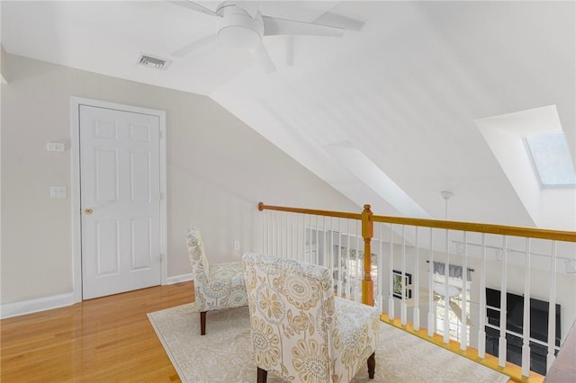 sitting room featuring vaulted ceiling with skylight, visible vents, baseboards, a ceiling fan, and light wood-style floors