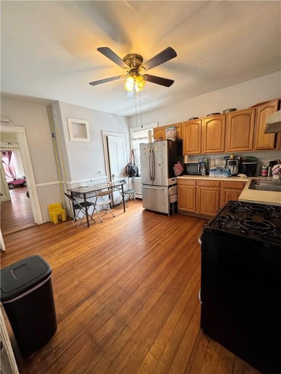 kitchen featuring sink, hardwood / wood-style flooring, ceiling fan, black appliances, and wall chimney exhaust hood