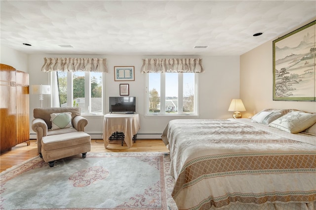 bedroom with multiple windows, a baseboard heating unit, and light hardwood / wood-style flooring