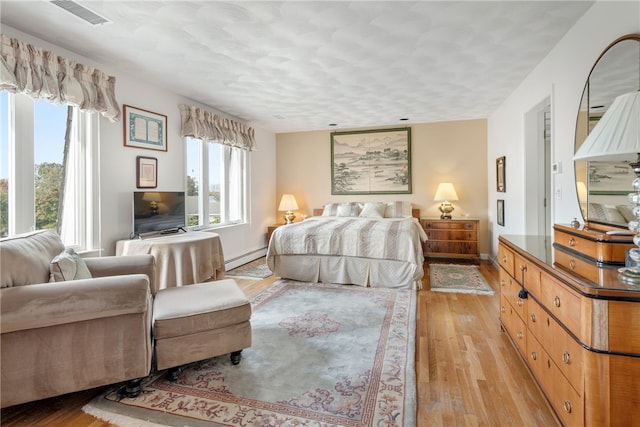 bedroom with a baseboard heating unit and light hardwood / wood-style floors