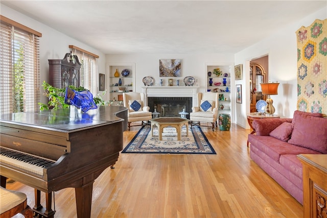 living room with built in shelves, a fireplace, and light wood-type flooring