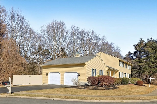 view of side of property with a garage, driveway, a chimney, and fence