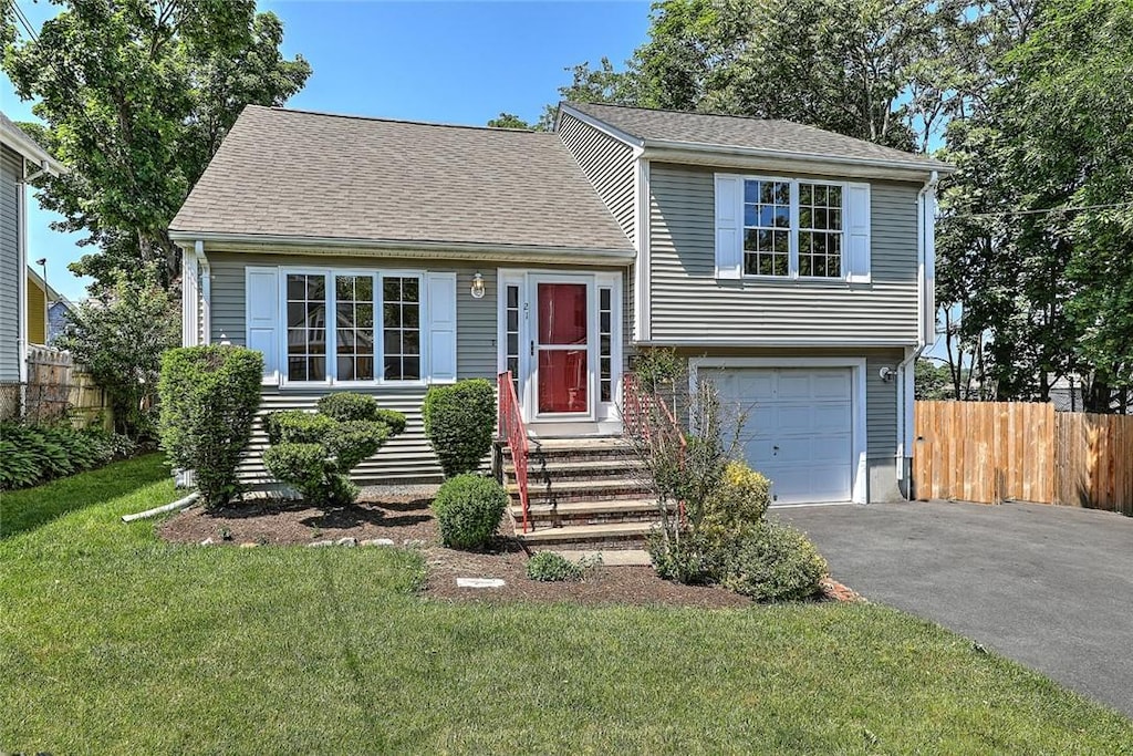 tri-level home featuring driveway, a shingled roof, an attached garage, and fence